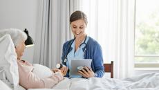 caregiver at patient bedside reviews prescription information with a virtual care prescriber on a tablet caregiver at patient bedside reviews prescription information with a virtual care prescriber on a tablet