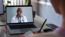 Female doctor on laptop smiles at patient in foreground who is taking notes Female doctor on laptop smiles at patient in foreground who is taking notes