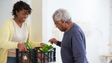 Woman holds a plastic delivery of prescription produce for an older man